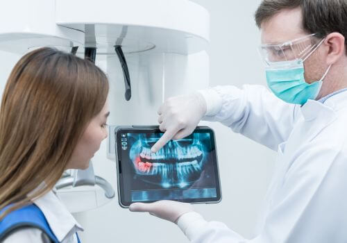 Dentist pointing at dental x-ray to show client a trouble spot.